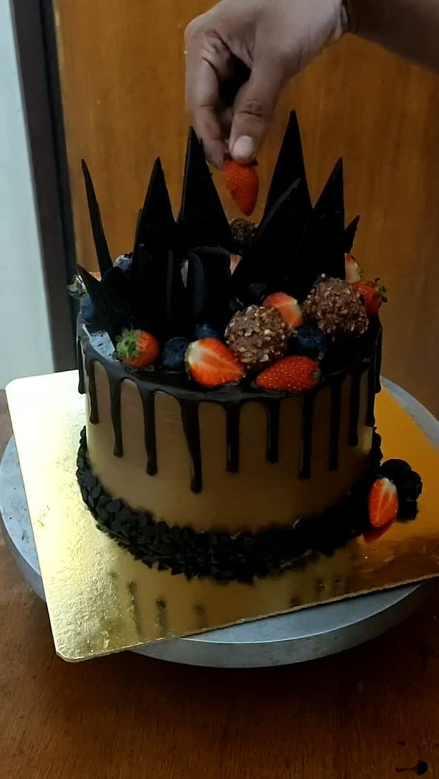 Strawberry being placed on a drip cake